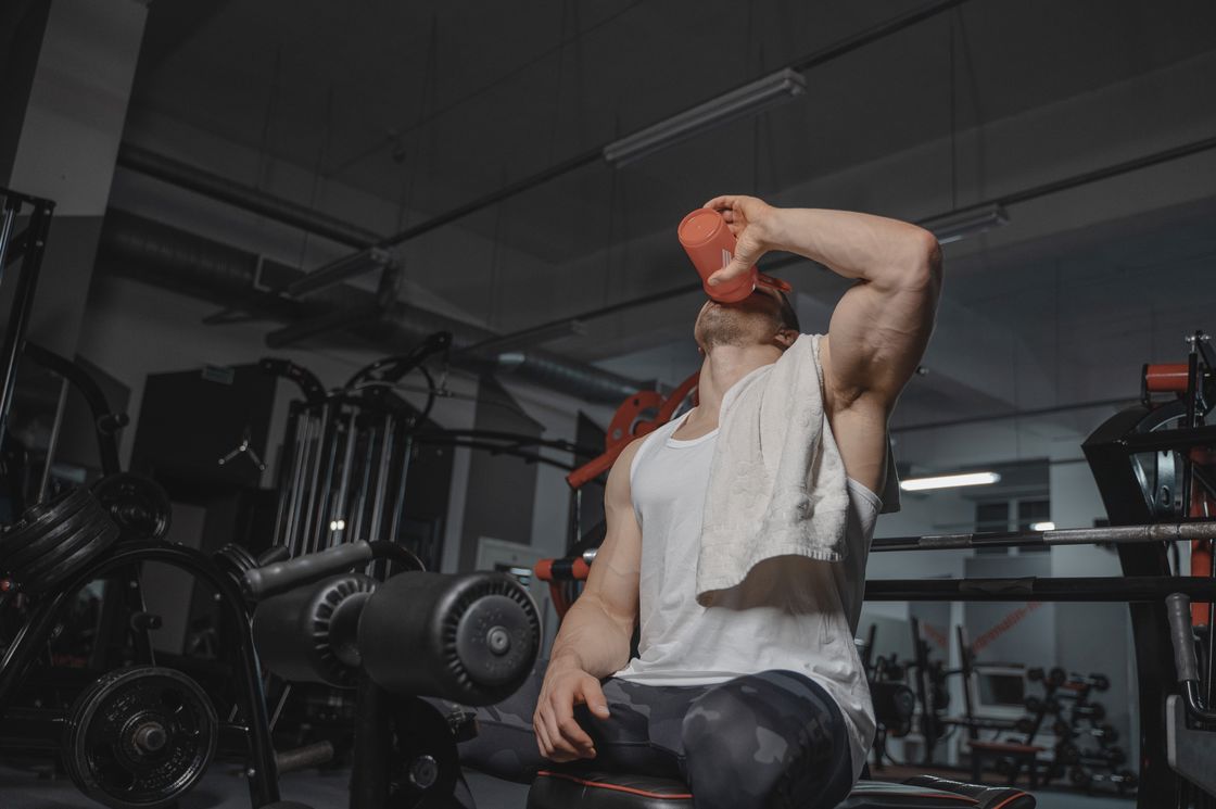 Man drinking from his orange tumbler while sitting down on an exercise equipment