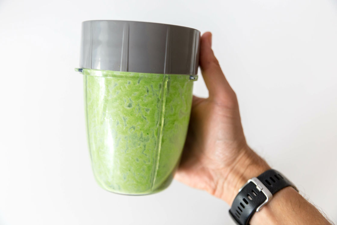 Person holding a Nutribullet mixture filled with green protein powder shake with the gray lid still covered