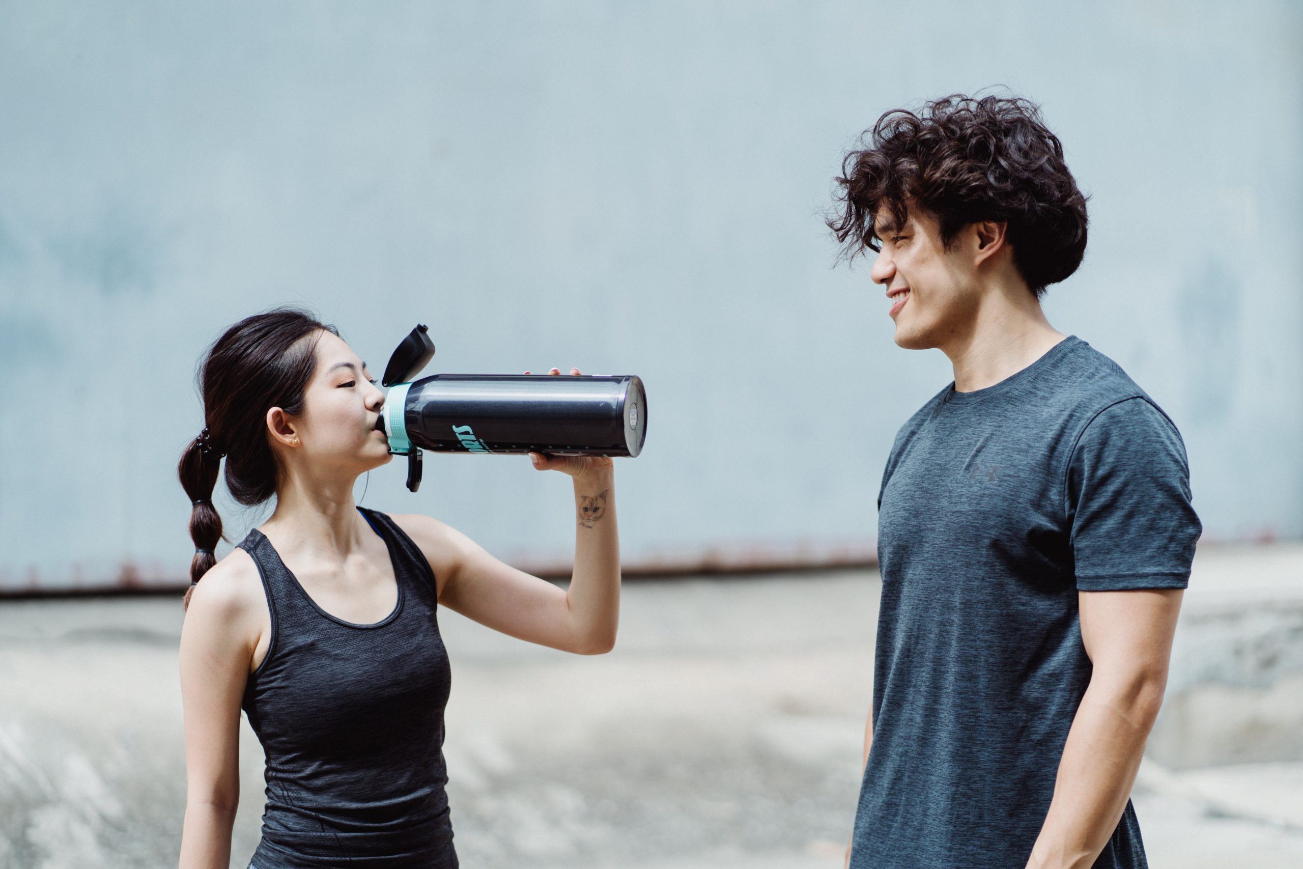 A woman drinking on a tumbler with a man smiling at her