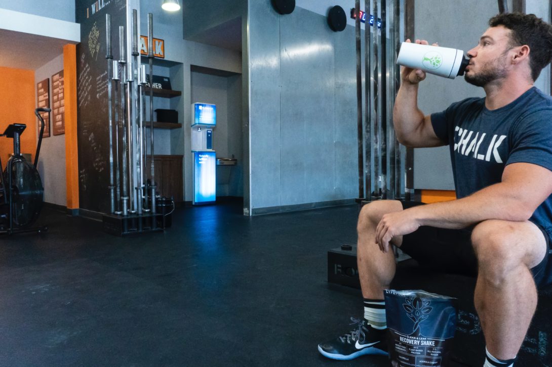 A man sitting and drinking on a white tumbler on the gym