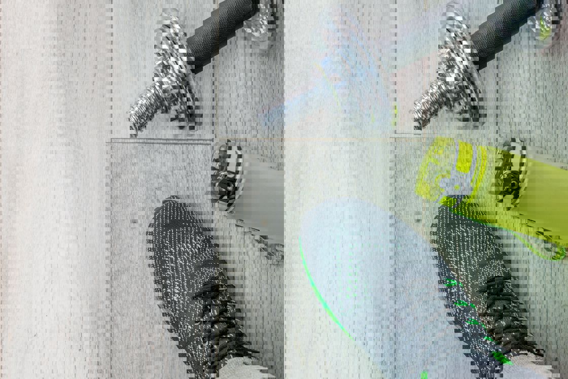 Close up of a man wearing gray sneakers, green water bottle and weights on the floor