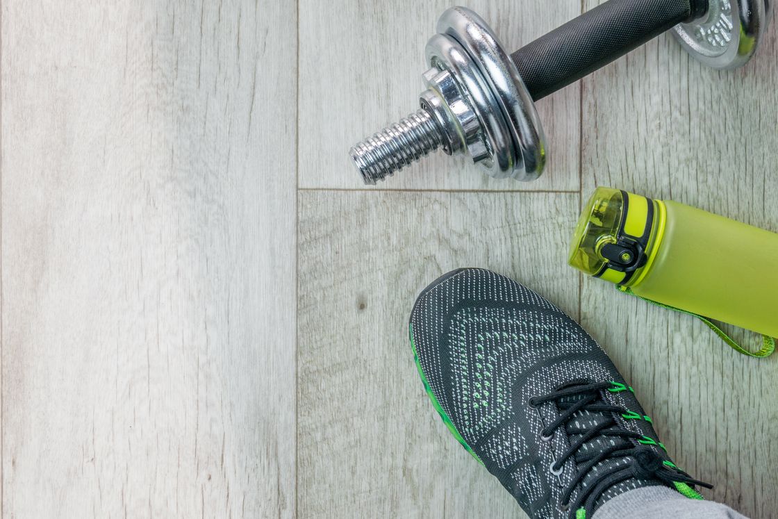 Close up of a man wearing gray sneakers, green water bottle and weights on the floor