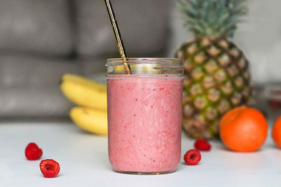 Whey powder mixed with red raspberries and fruits in a clear glass bottle and metal straw