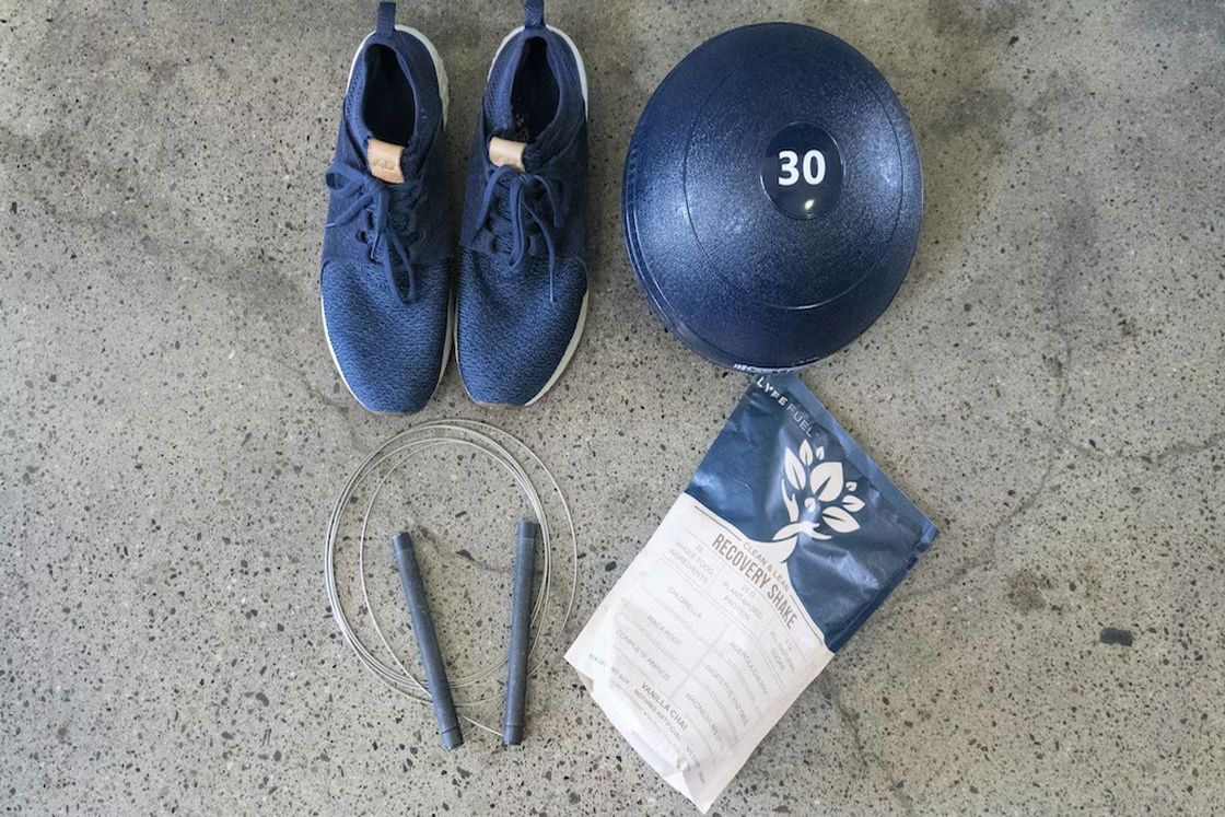 Blue sneakers, jump rope, ball and a bag of protein powder placed on the floor