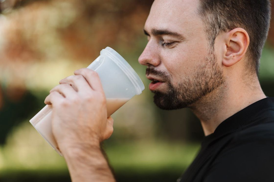 Man drinking his mixed protein powder from a plastic tumbler