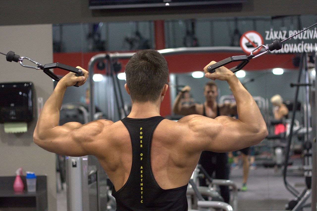 A man wearing a black tank top is using the black pull rope inside a well-lit gym.