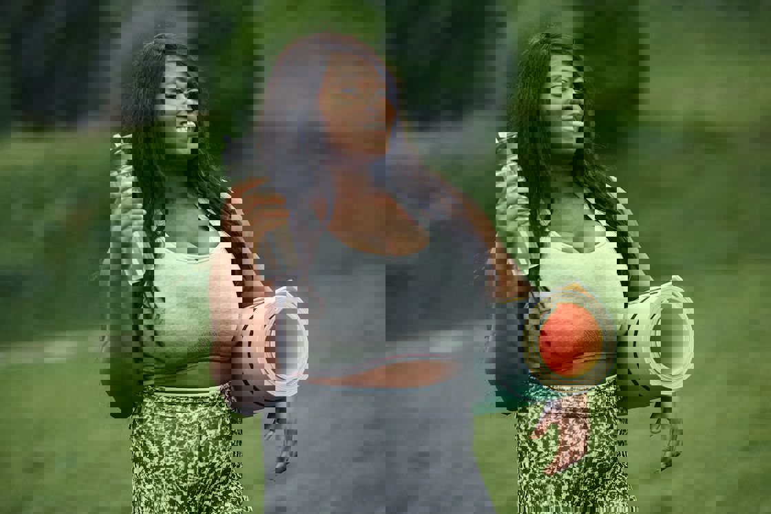 Woman wearing a sports bra and leggings while holding a water bottle and yoga mat in each hands