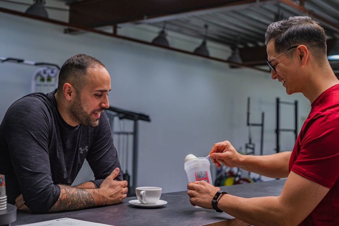 Man scooping out a creatine powder into a tumbler as his friend looks on