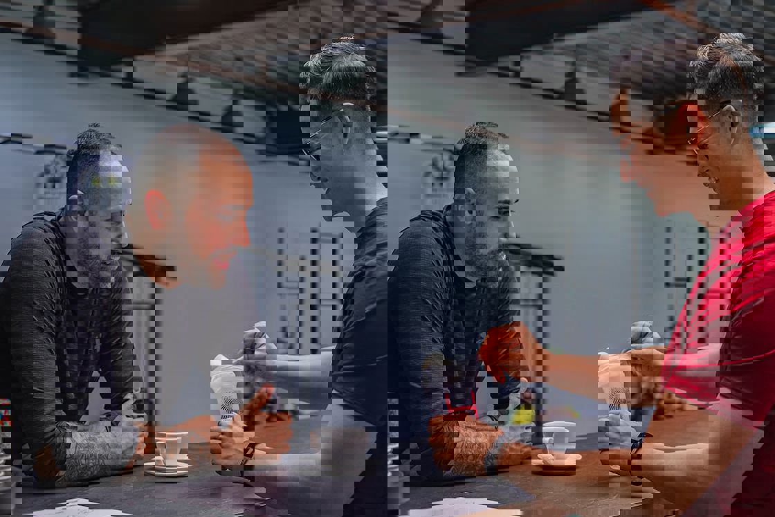 Man scooping out a creatine powder into a tumbler as his friend looks on