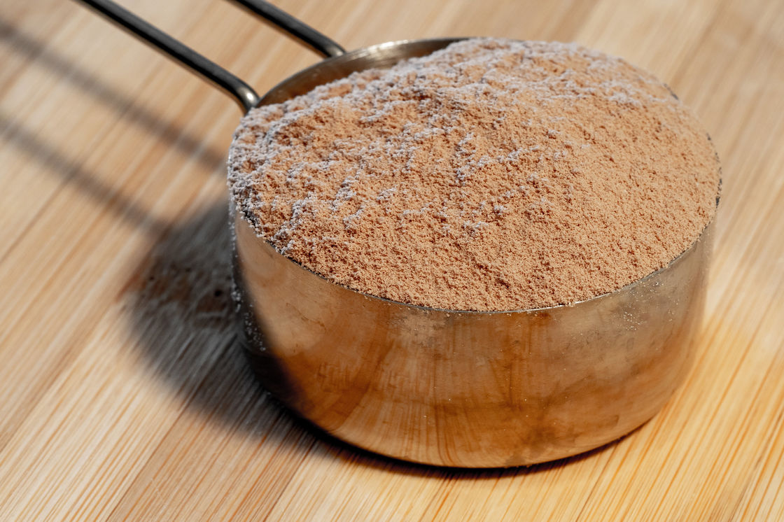 Chocolate flavored whey protein powder in a bronze scoop