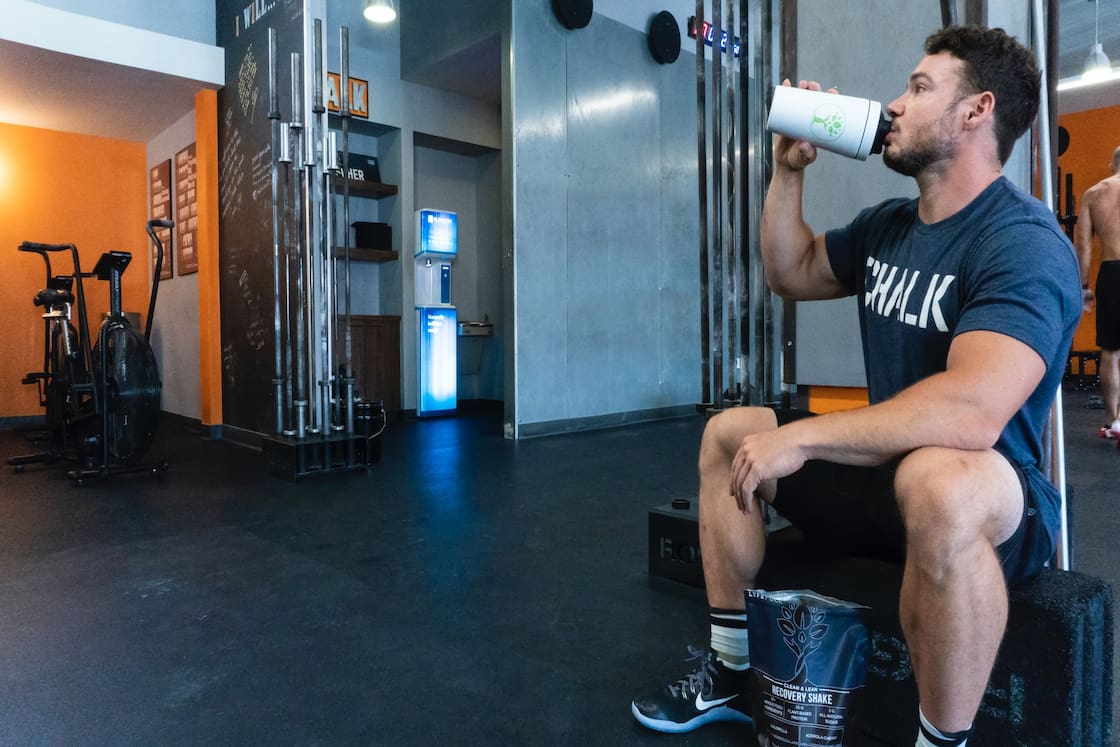 A man wearing a blue shirt and black shorts is drinking from a white tumbler