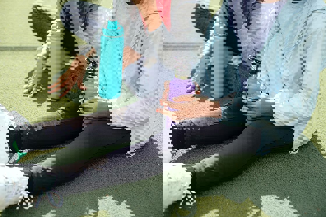 Two women sitting on artificial grass while holding their water tumblers