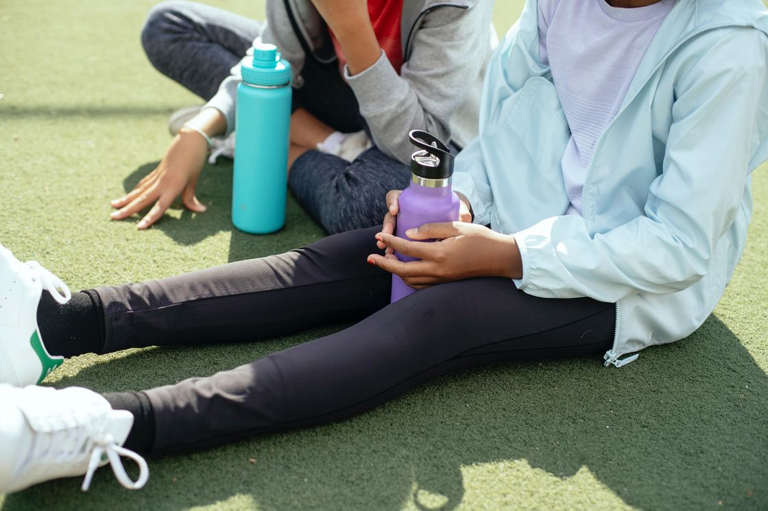 Two women sitting on artificial grass while holding their water tumblers