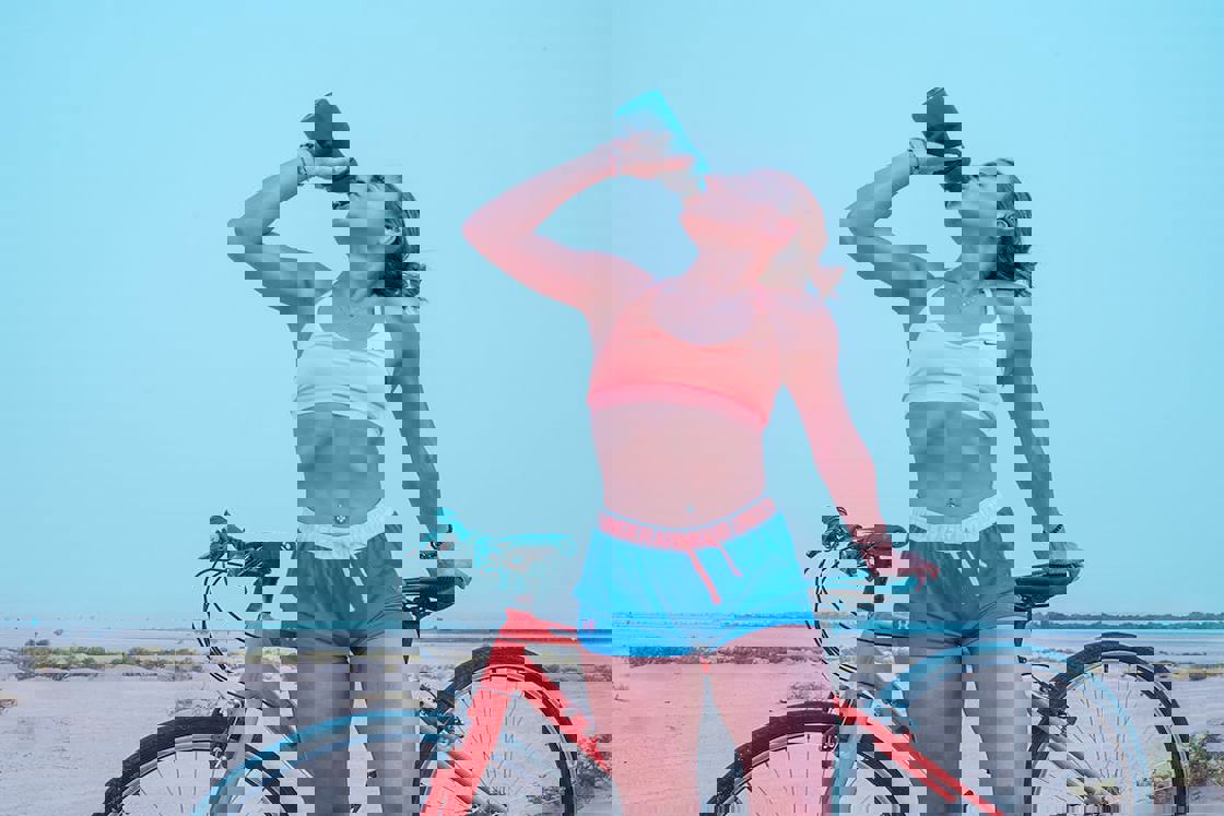 Woman drinking from her water bottle while holding on to her bicycle