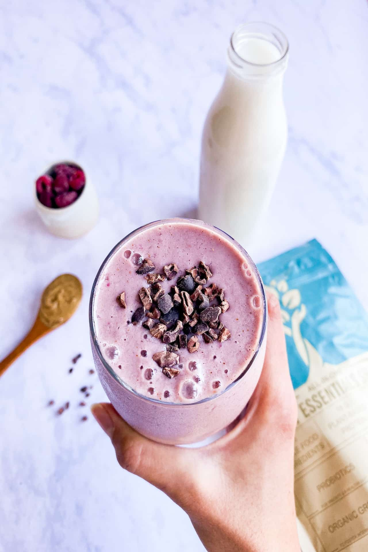 A person holding a pink strawberry shake near a glass of milk on top of a marbled table