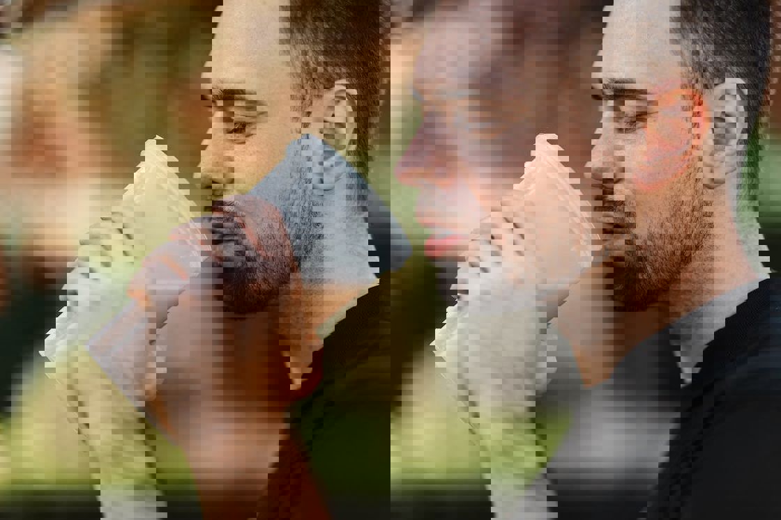 Man drinking his protein shake from a clear plastic tumbler during his break while exercising outdoors