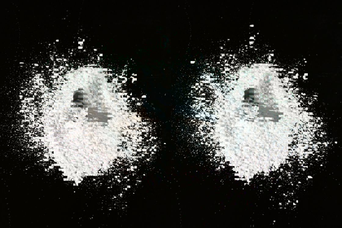 White powder spilled on a black table with a gray scooper on top of it