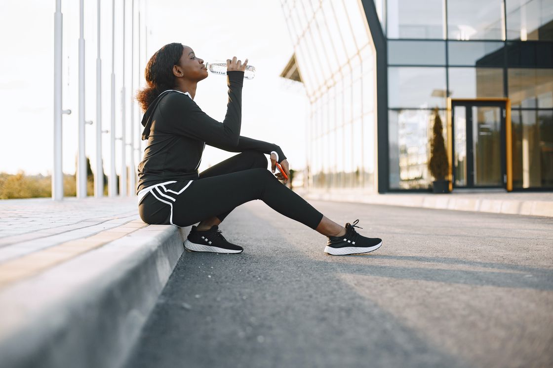 Woman sitting down on the side of a road while drinking from a water bottle