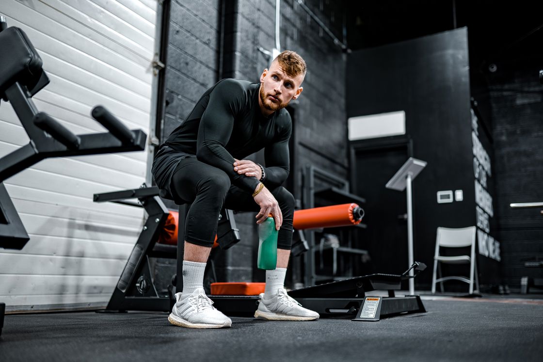 Man holding a green water bottle while sitting down on a gym equipment