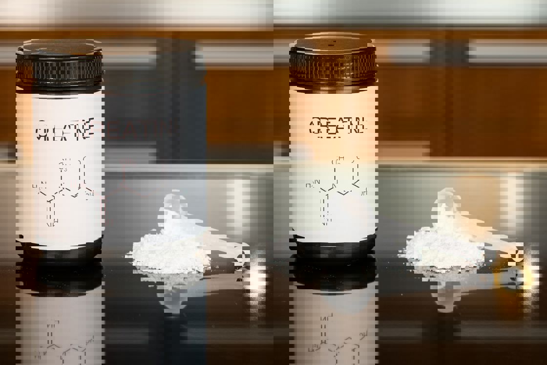 Creatine bottle with a scoop of powder spilling on the side