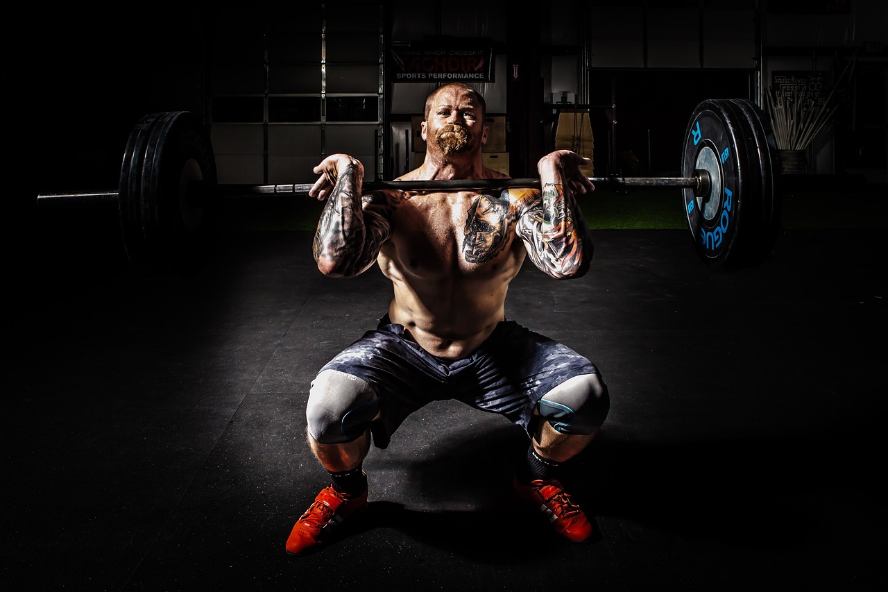 A topless man wearing black shorts and red shoes is lifting weights on a black rubber floor