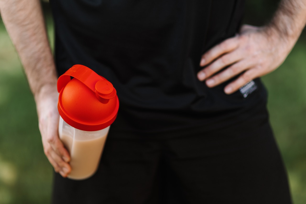 A person wearing black shirt and black shorts is holding a sports bottle with red lid