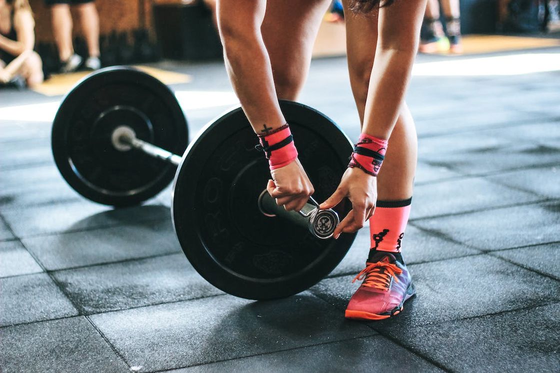 Woman fixing the lock of a barbell before lifting it from the gym floor