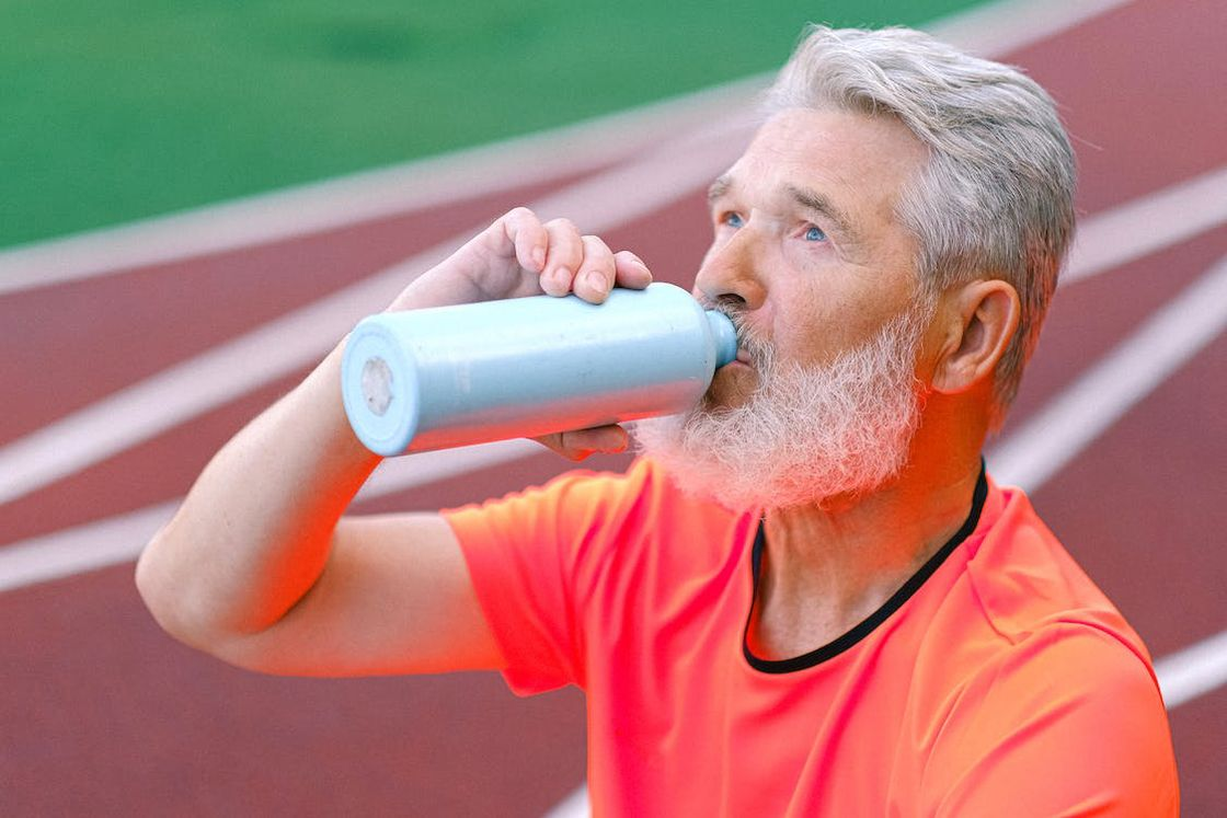 Man sitting on a track field while drinking from his blue aluminum bottle
