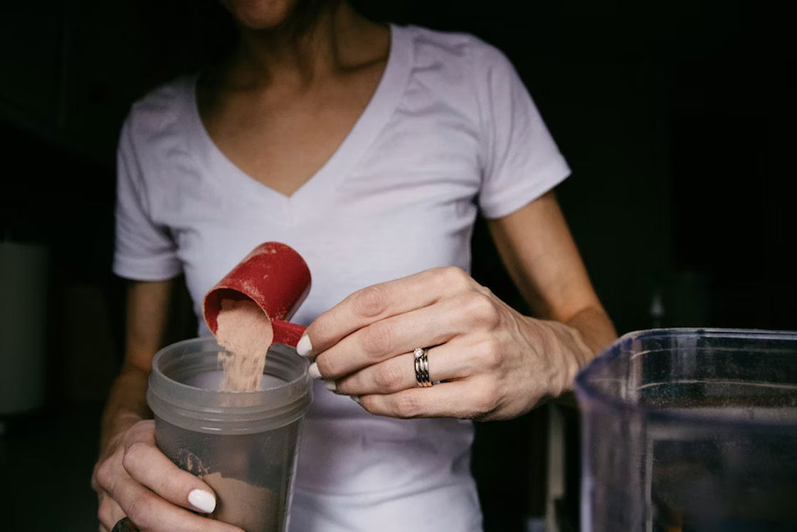 Woman pouring a scoop of protein powder into a plastic tumbler