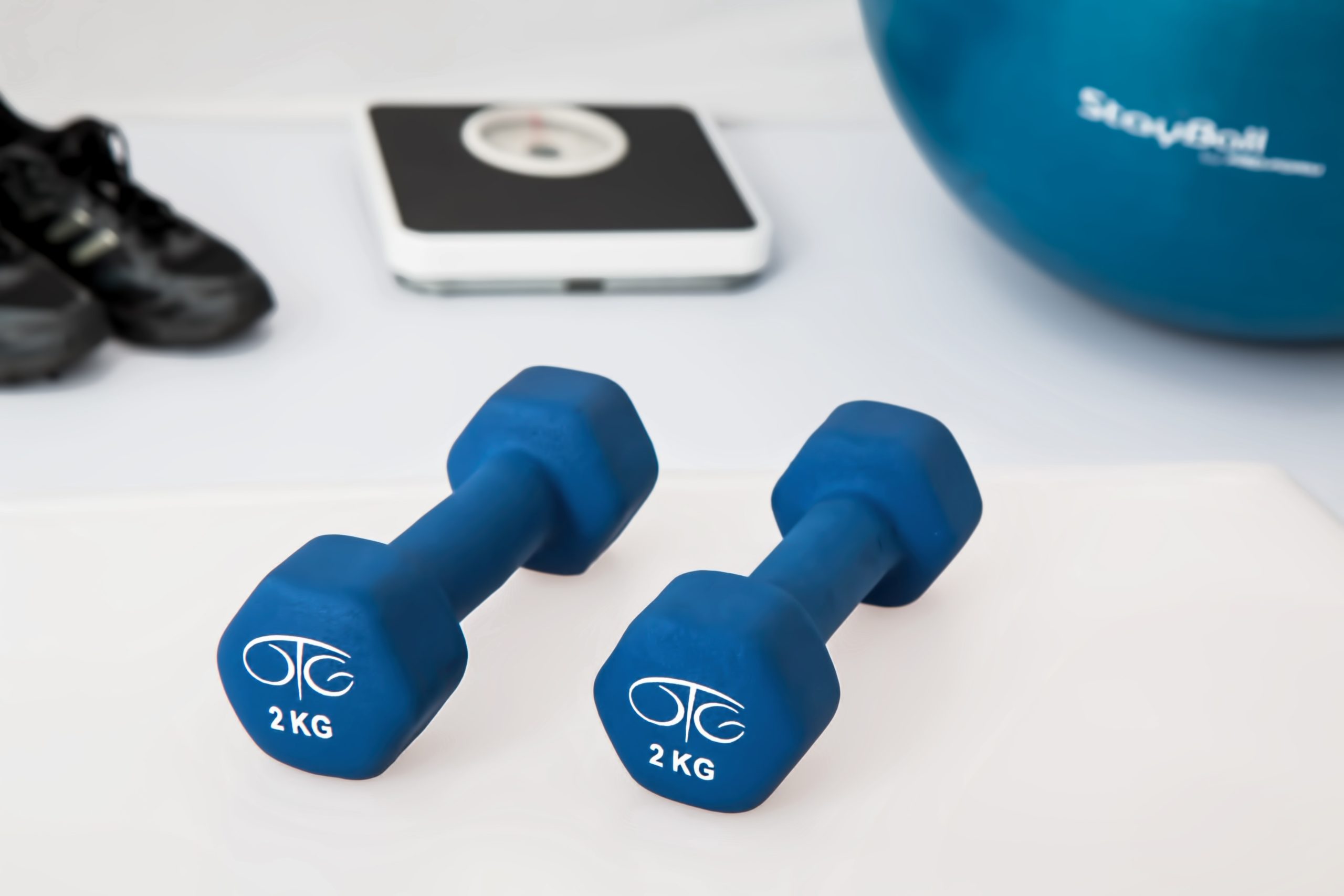 A pair of blue dumbbell with shoes, weighing scale. and exercise ball on the background