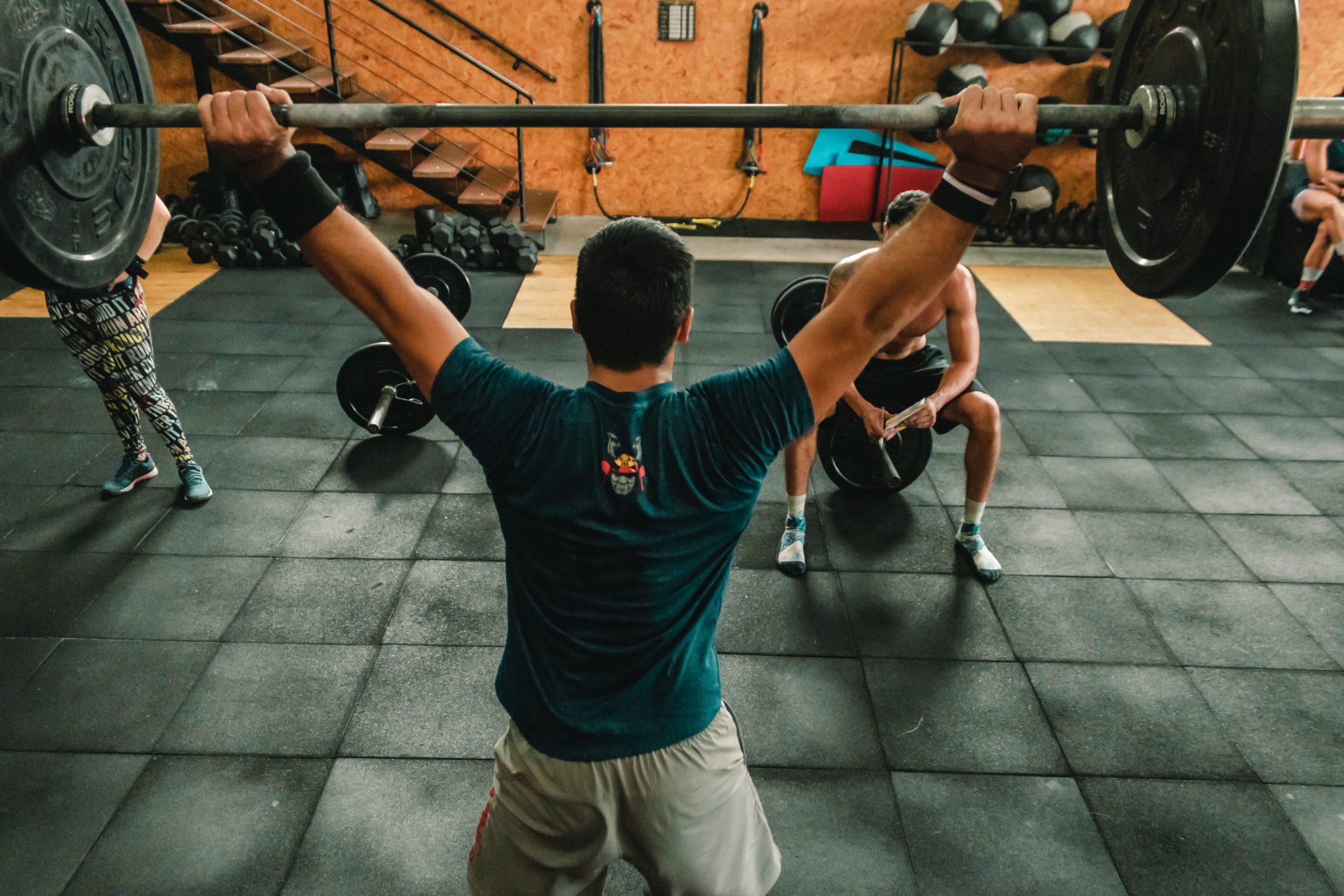 A man lifting a barbell in front of a man and a woman