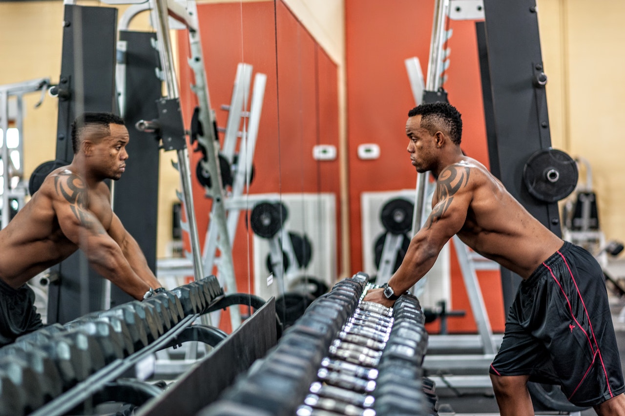 A man wearing black shorts is holding a silver and black dumbbell in front of a clean mirror