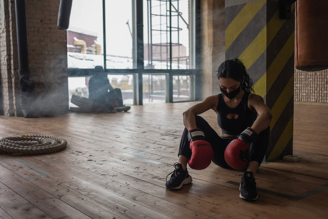 Woman wearing boxing gloves slumped down on the gym floor after a tiring session