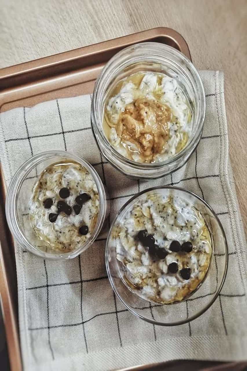 Three clear glasses of protein with oatmeal and chia seeds on a brass-colored tray on top of a brown wooden table