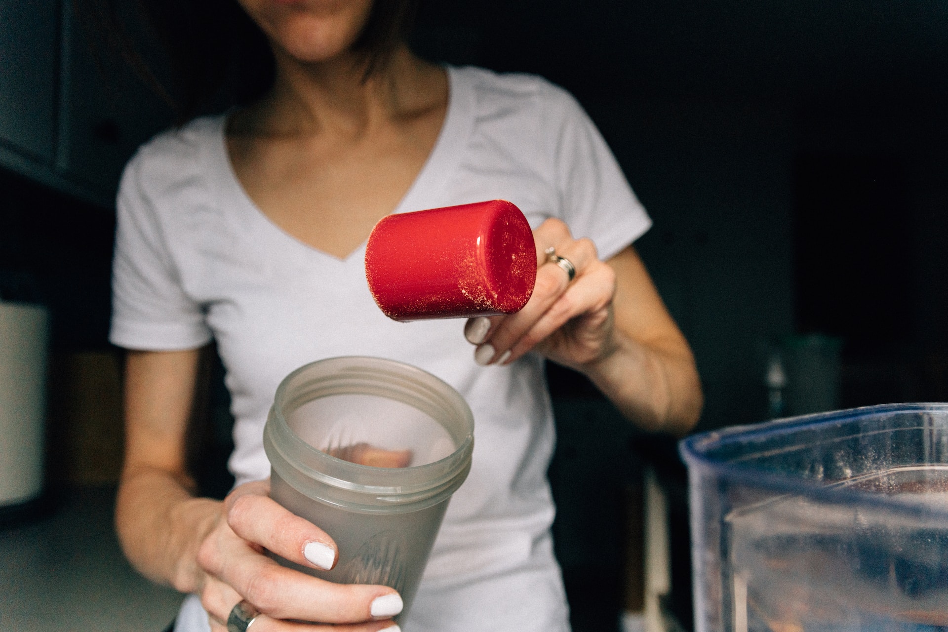 A woman wearing a white v-neck shirt is holding a red scoop and plastic tumbler