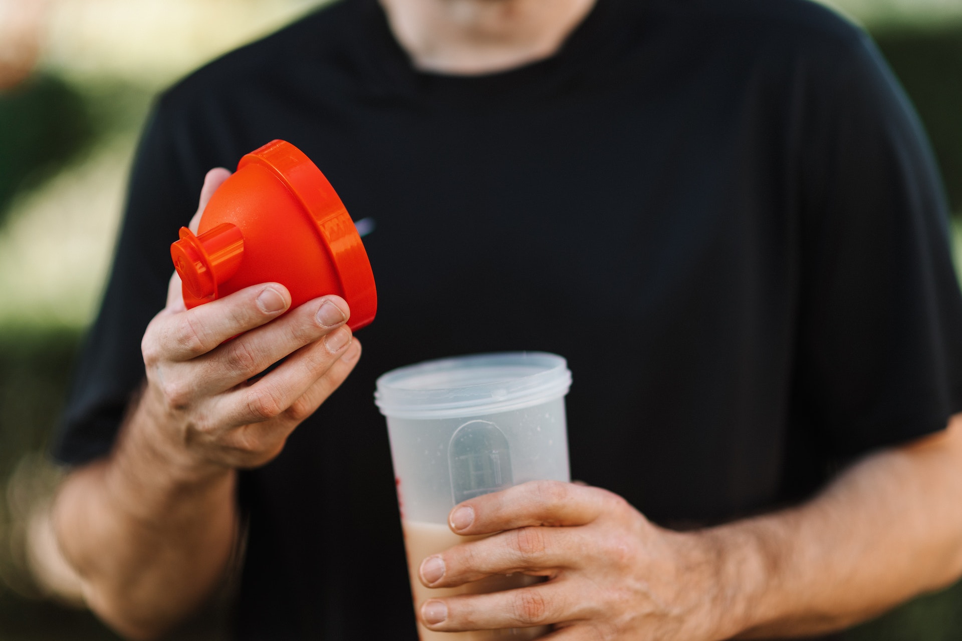 A man wearing black shirt is holding a red lid and plastic tumbler