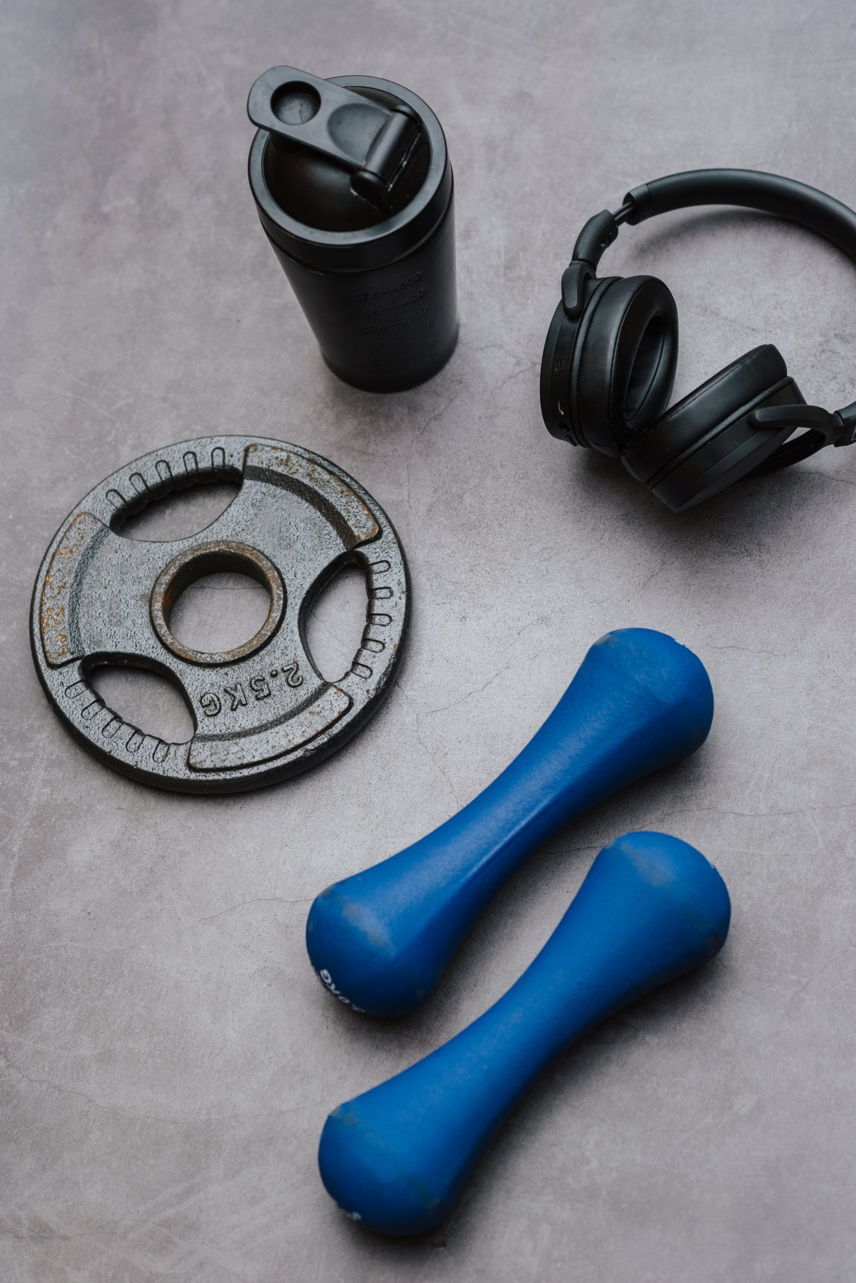 Weights, headphones, and a water bottle on a concrete floor